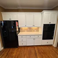 Modern kitchen with white cabinets, black appliances, wooden floors, and under-cabinet lighting over a tile backsplash.