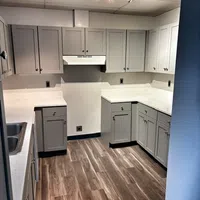Modern kitchen with light gray cabinets, white countertops, stainless steel sink, and wood-look flooring under spotlight.
