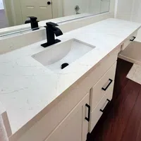 Modern white bathroom vanity with black faucet, white marble countertop, and dark wood flooring.