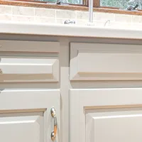 Close-up of white kitchen cabinets with silver handles under a beige tiled backsplash and countertop.