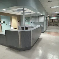 Empty hospital nurse station with gray counters in a wide hallway with closed doors and ceiling lights.