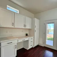 Bright modern kitchen with white cabinets, black handles, dark wood floor, and a glass door leading outside.