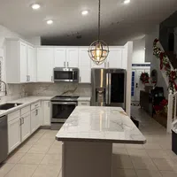 Modern kitchen with white cabinets, marble countertops, stainless steel appliances, and a decorative hanging light fixture