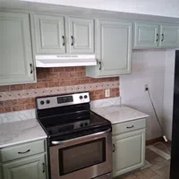Modern kitchen with stainless steel stove, white marble countertops, sage green cabinets, and brown tiled backsplash.