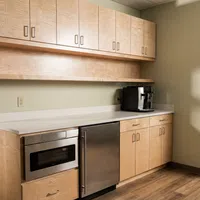 Modern kitchen area with wooden cabinets, stainless steel microwave and fridge, and coffee maker on countertop