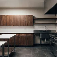 Modern professional kitchen with stainless steel appliances, wooden cabinets, and white countertops on tiled floor.