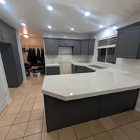 Modern kitchen with dark gray cabinets, large white quartz island, tiled floor, and recessed ceiling lights