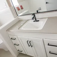 Modern white bathroom vanity with black faucet, tiled countertop, and matching black cabinet handles.