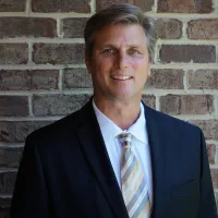 a man wearing a suit and tie standing in front of a brick wall