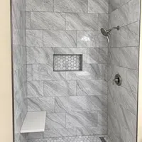 Modern shower with marble tile walls, hexagonal floor tiles, built-in shelf, bench, and handheld showerhead.