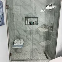 Modern bathroom shower with glass door, marble tiles, built-in shelf, and folded towels on bench.