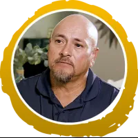 Middle-aged bald man with goatee wearing a navy blue shirt inside a gold circular frame.