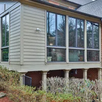 Modern house extension with large glass windows and brick exterior supported by columns above shrubbery.