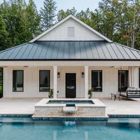 Modern pool house with metal roof, pool, hot tub, and swing surrounded by trees and greenery.