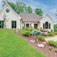 White brick house with large windows surrounded by lush green lawn and landscaped garden beds