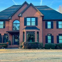 Two-story brick house with black shutters, large windows, and a decorated front door in winter daylight.