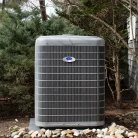 Carrier Infinity outdoor air conditioning unit installed on concrete pad surrounded by rocks and greenery