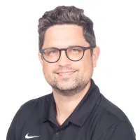 Man with glasses wearing a black Nike polo shirt with PV Heating Cooling Plumbing logo smiling against white background