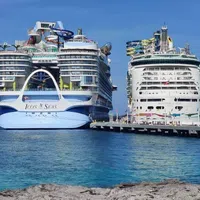 Two large cruise ships docked side by side at a pier with clear blue water and sky.
