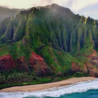 Dramatic green cliffs rising above a sandy beach and ocean waves under a cloudy sky