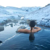Person relaxing in a hot spring surrounded by snow-covered rocky landscape under clear sky