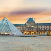 Sunset view of the Louvre Museum with its glass pyramid and historic architecture in Paris, France.