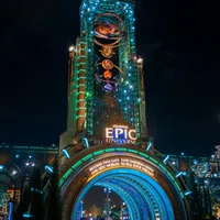 Universal Epic Universe entrance gate illuminated at night with colorful lights and visitors walking through.