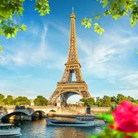 Bright Eiffel Tower by the Seine River with boats, framed by green leaves and pink flowers on a sunny day.