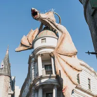 Large dragon sculpture perched on Gringotts Bank building in a theme park under clear blue sky.