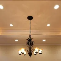 Elegant chandelier with six glowing lights hangs from a ceiling with recessed lighting and crown molding.