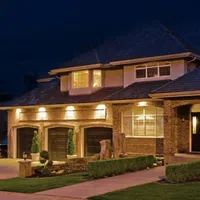Large illuminated suburban brick house with three-car garage and well-maintained landscaping at night
