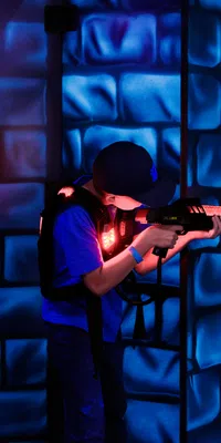 Child playing laser tag indoors with neon blue and orange lights in a futuristic arena environment.