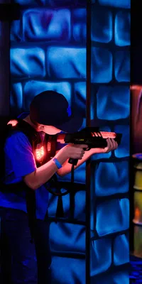 Child playing laser tag indoors with neon blue and orange lights in a futuristic arena environment.