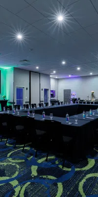 Modern conference room with U-shaped table setup, black chairs, blue and green patterned carpet, and abstract logo on screen.
