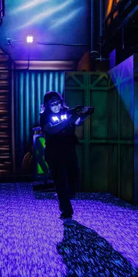 Person playing laser tag in neon-lit maze with glowing walls and dark ambient lighting indoor arena
