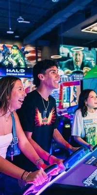 Four young adults enjoying playing arcade games in a colorful, lively game center with neon lighting.