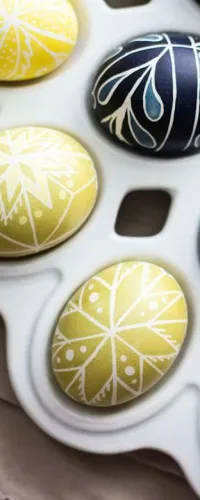 Yellow and blue Easter eggs with white intricate patterns arranged in a plastic egg tray on a cloth.