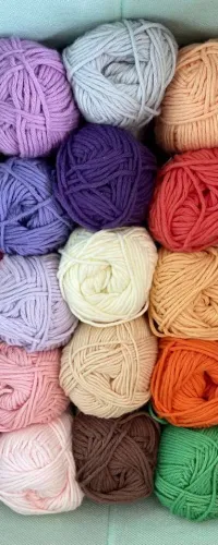 Box of colorful yarn balls neatly arranged in rows showcasing various shades and textures for knitting or crocheting.