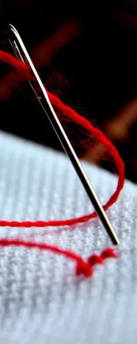 Close-up of a silver needle with red thread piercing white fabric in sewing or embroidery.