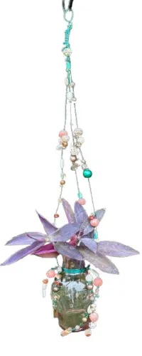 Hanging glass vase with purple foliage decorated with colorful beaded strings on white background