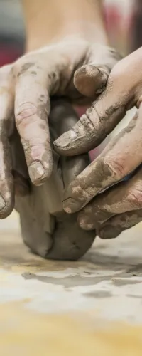 Close-up of hands shaping wet clay on a wooden table during pottery making process.