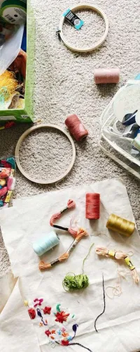 Embroidery threads, hoops, and fabric with colorful floral stitching spread on a carpeted floor for a sewing project.