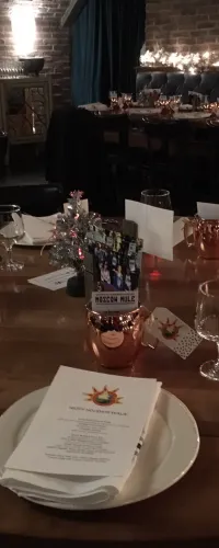 Elegant restaurant table set with menus, copper mugs, glassware, and festive centerpiece under warm brick wall lighting
