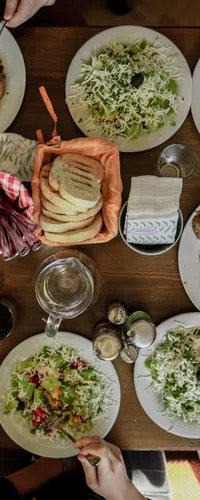 Overhead view of a wooden table with plates of meat, rice, salad, bread, and drinks being shared by diners.