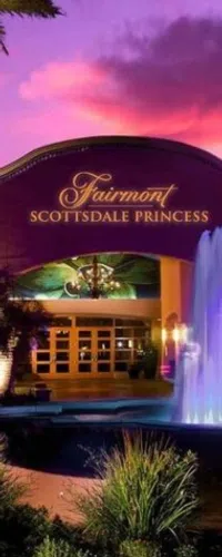 Entrance of Fairmont Scottsdale Princess hotel at sunset with illuminated fountain and pink-purple sky.