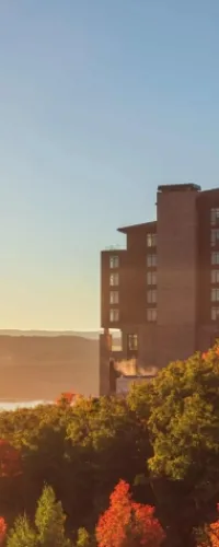 Modern brick building overlooking colorful autumn trees under a clear blue sky at sunset.