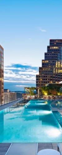 Rooftop infinity pool overlooking city skyline at sunset with clear blue sky and modern buildings.