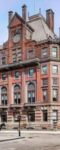 Red brick Victorian building with arched windows, decorative stone detailing, and a large clock on the facade
