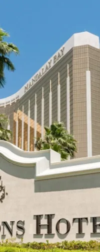 Mandalay Bay hotel building with blue sky and palm trees, partial signage of Tropicana Las Vegas Hotel.