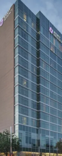 Modern high-rise office building with glass facade and brown paneling under a cloudy sky.